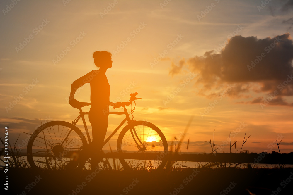 Fototapeta premium Silhouette of happy women with bicycle in nature at the sky sunset