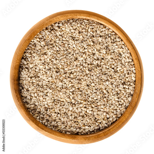 Natural white sesame seeds in wooden bowl. Unpeeled dried fruits of Sesamum, also called benne. Oilseed crops. Isolated macro food photo close up from above on white background.