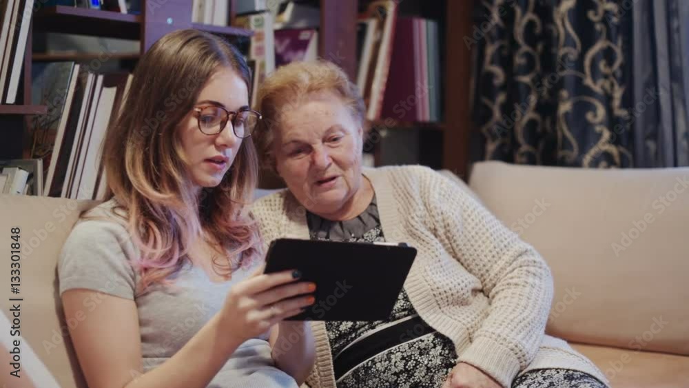 Cheerful young girl with an elderly woman playing together with digital tablet at home Cheerful young girl with an elderly woman playing together with digital tablet at home