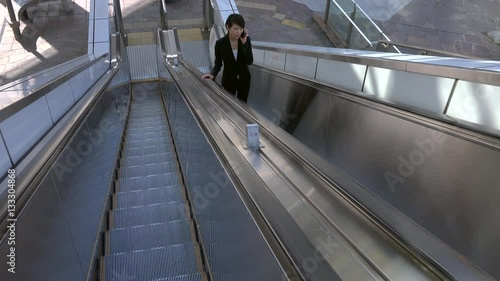 Happy beautiful Japanese female manager speaking on cell phone. Asian businesswoman, confident girl, busy woman talking with smartphone, mobile telephone on escalator during break