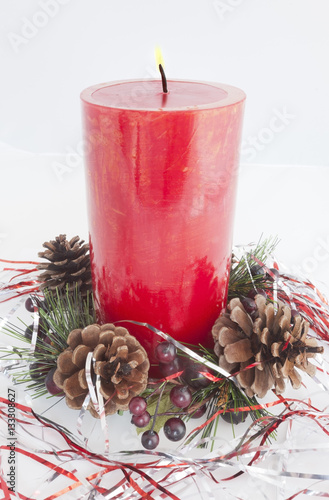 Red holiday candle WITH FLAME with pine cones and tinsel at the base. Vertical.