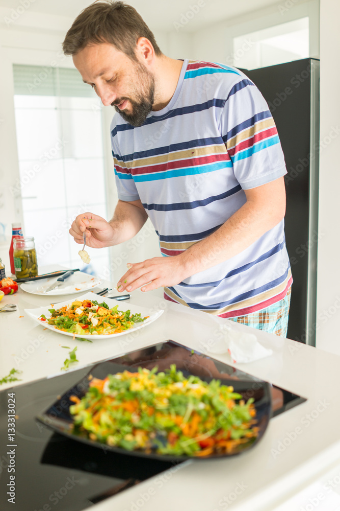 Handsome man cooking at home preparing salad in kitchen