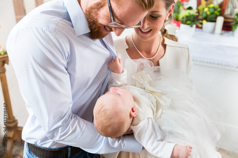 Fototapeta premium Junge Eltern mit ihrem Baby im Taufkleid in einer Kirche