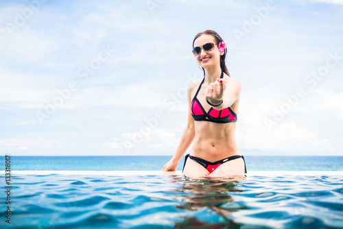 Tablou pe pânză Woman making wooing gesture at edge of infinity pool