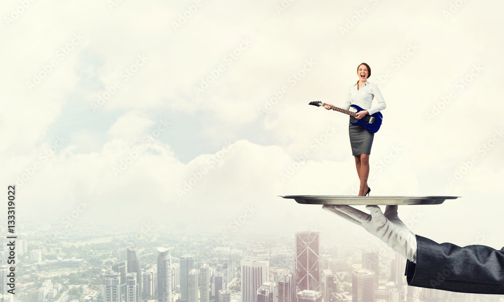 Attractive businesswoman on metal tray playing acoustic guitar against cityscape background Attractive businesswoman on metal tray playing acoustic guitar against cityscape background