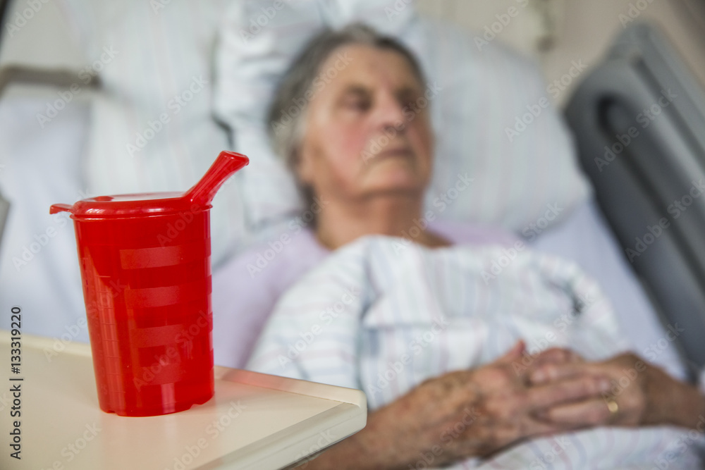 Seniorin im Krankenhaus trinkt aus einer Schnabeltasse Seniorin im Krankenhaus trinkt aus einer Schnabeltasse