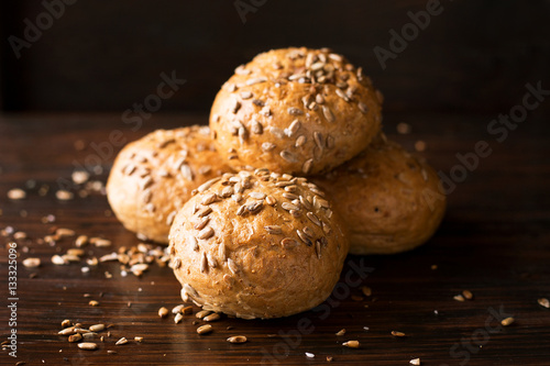 Four buns with seeds on a dark wooden background, top view