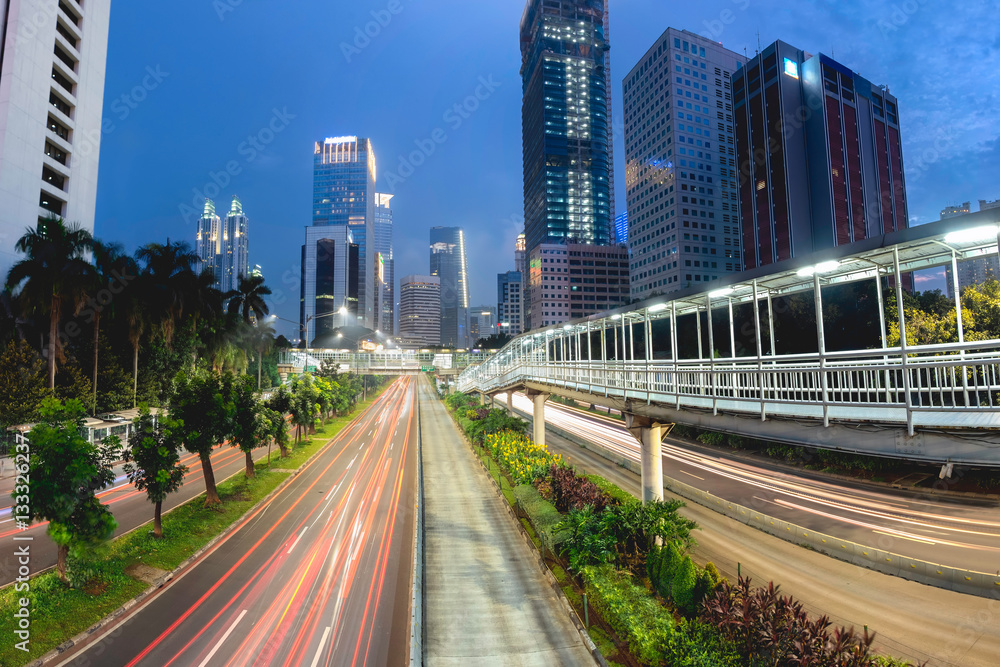 Fototapeta premium Light trail of vehicle traffic in Jakarta main road, Sudirman Street, Jakarta. Also showing row of beautiful pedestrian bridge in the middle of the road. Urban Skyline, Building Exterior