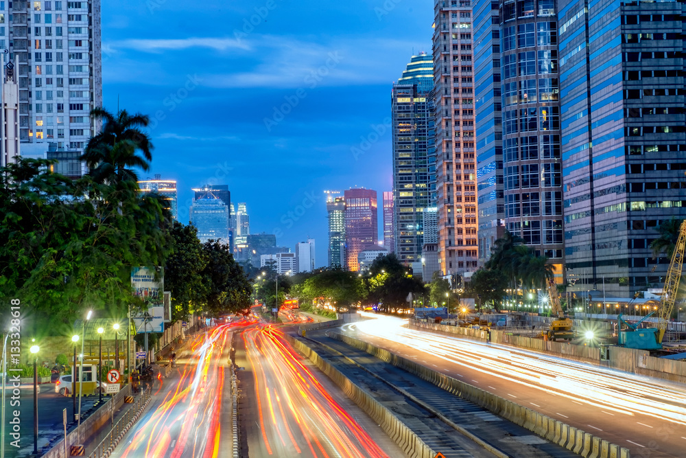 Iconic skyline and light trail of heavy traffic in Sudirman Street, Jakarta, Indonesia at dusk, showing light trail of busy traffic and iconic skyscrapers in Jakarta. Urban Skyline Iconic skyline and light trail of heavy traffic in Sudirman Street, Jakarta, Indonesia at dusk, showing light trail of busy traffic and iconic skyscrapers in Jakarta. Urban Skyline