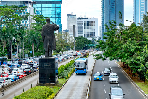 View of  modern skyscraper buildings and public transport bus  in front of general Soedirman statue. In the central business area in Sudirman street, Jakarta, Indonesia
