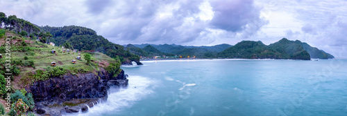 Beautiful panorama  of cliff, beach, hill and sea in cloudy day. Wave splashed when hit the cliff and little hut in the top of the cliff.   Captured on Lampon Beach, Kebumen, Indonesia photo