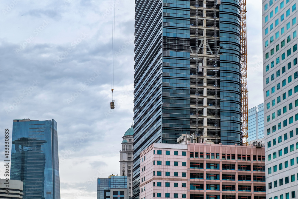 Photo of skyscrapper building under construction, when the builder lifting construction material into the top using crane. Captured in Jakarta, Indonesia