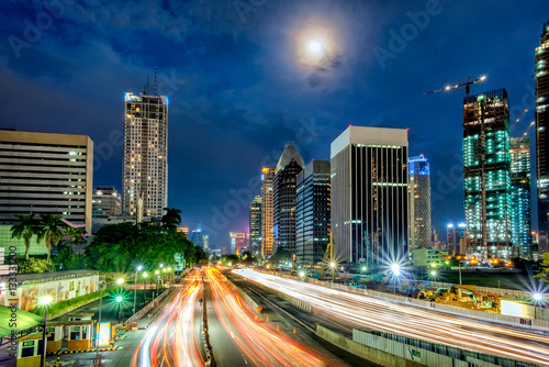 Iconic skyline and light trail of heavy traffic in Sudirman Street, Jakarta, Indonesia at dusk, showing light trail of busy traffic and iconic skyscrapers in Jakarta, iluminated by moon light
