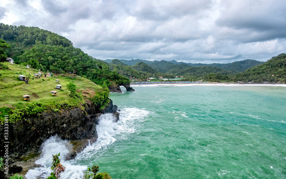 Beautiful scenery of cliff, beach and sea in cloudy day. Wave splashed when hit the cliff and little hut in the top of the cliff.   Captured on Lampon Beach, Kebumen, Indonesia