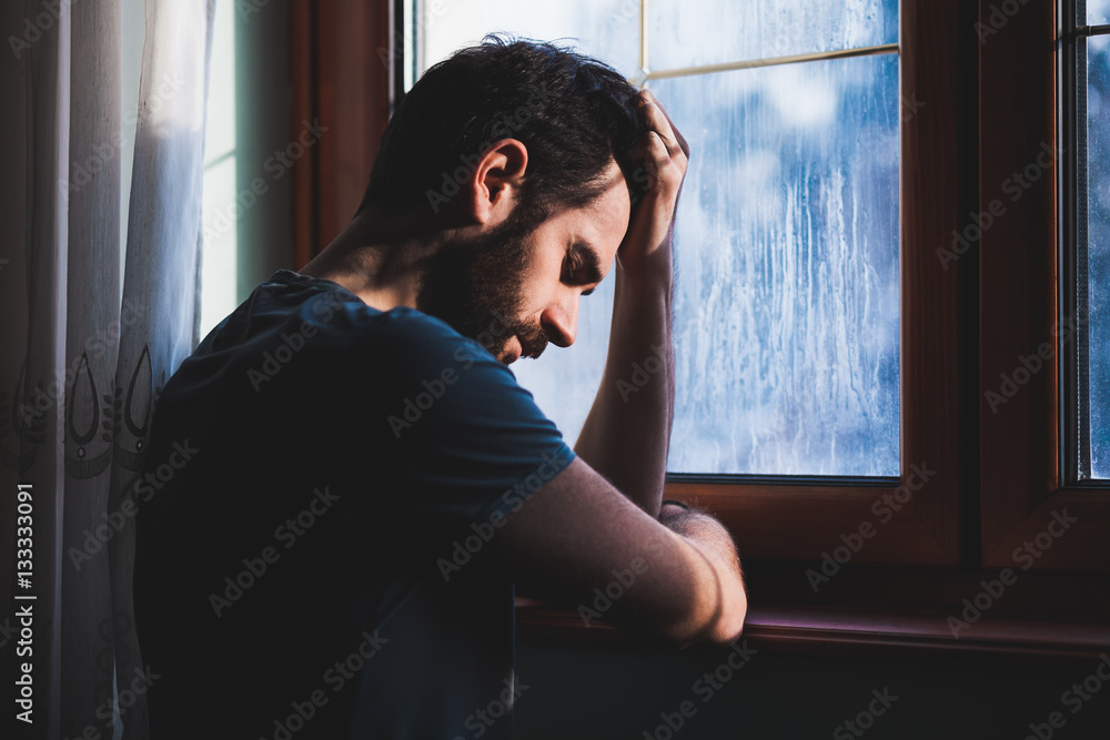 Young sad mad sitting by the window in regret Young sad mad sitting by the window in regret