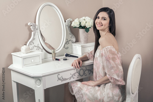 Valokuvatapetti Beautiful happy woman with pink dress and long black hair in her room near her dressing table posing before party