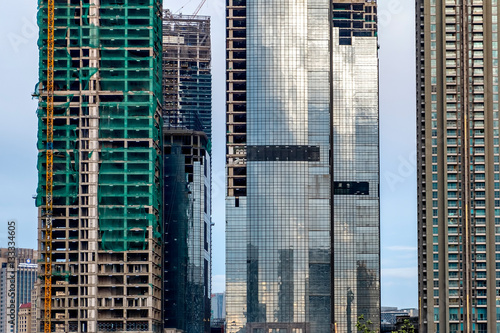 Skyscraper building in between another buildings, the building is unifinished andunder construction also show glass window on skyscraper, showing reflection of sky and building in Jakarta, Indonesia photo