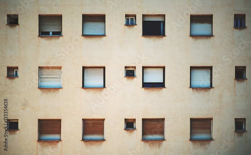 Beige facade of residential building in Barcelona with regular pattern of windows of different size, streaks of rust under the sills