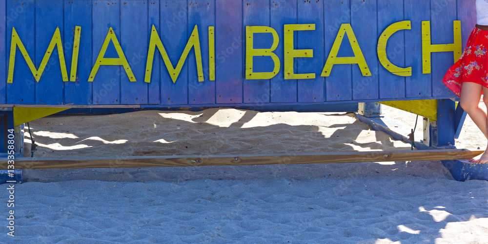 Fototapeta premium Miami Beach sign on a sandy beach in Florida, USA. The beach famous stop for a memorable picture.