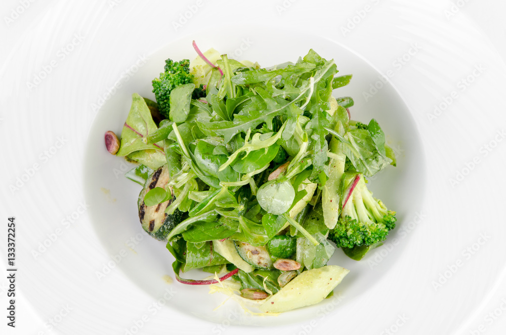 Salad of green vegetables with broccoli, zucchini and walnut dressing on a plate on a white background, closeup Salad of green vegetables with broccoli, zucchini and walnut dressing on a plate on a white background, closeup