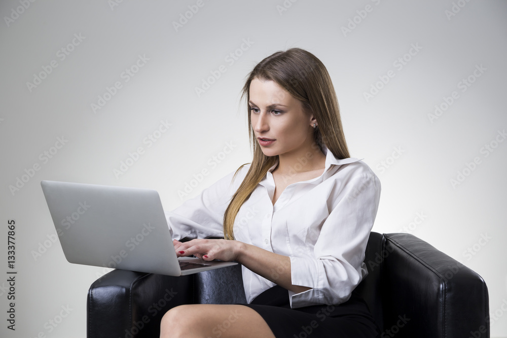 Portrait of a beautiful serious businesswoman in a white blouse sitting in a leather armchair with her laptop. Portrait of a beautiful serious businesswoman in a white blouse sitting in a leather armchair with her laptop.