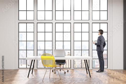 CEO at his workplace with white desk, an office chair and a transparent yellow visitor chair. Large windows are in the background. 3d rendering.