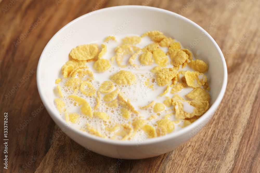 corn flakes with milk in white bowl on wood table, simple healthy breakfast