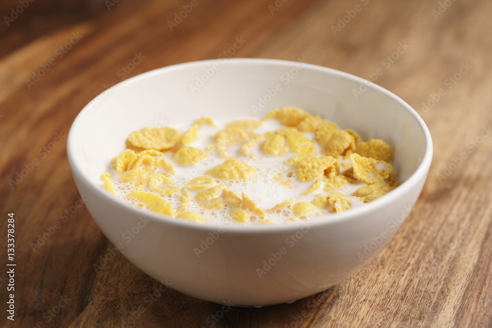 corn flakes with milk in white bowl on wood table, simple healthy breakfast corn flakes with milk in white bowl on wood table, simple healthy breakfast