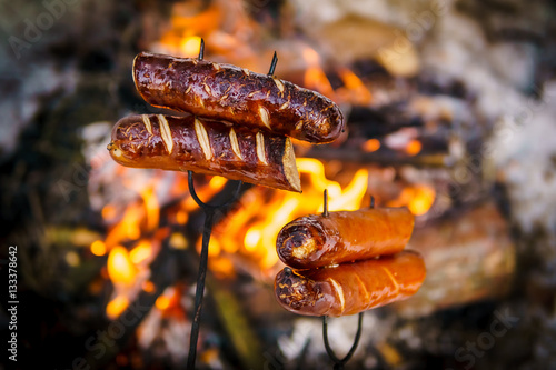 Obraz na płótnie delicious sausages baked on a campfire in the forest w salonie