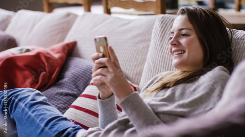 Attractive young woman relaxing at home on her couch using her cell phone