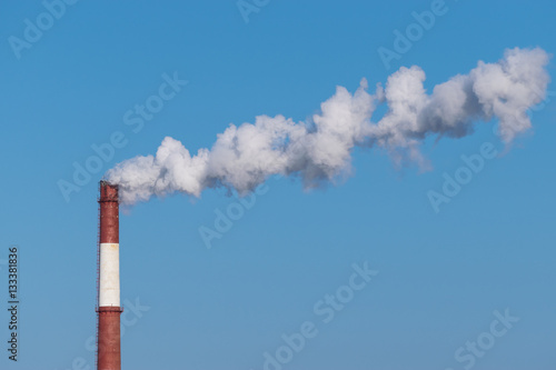 Industrial pipe with smoke on a blue sky background.