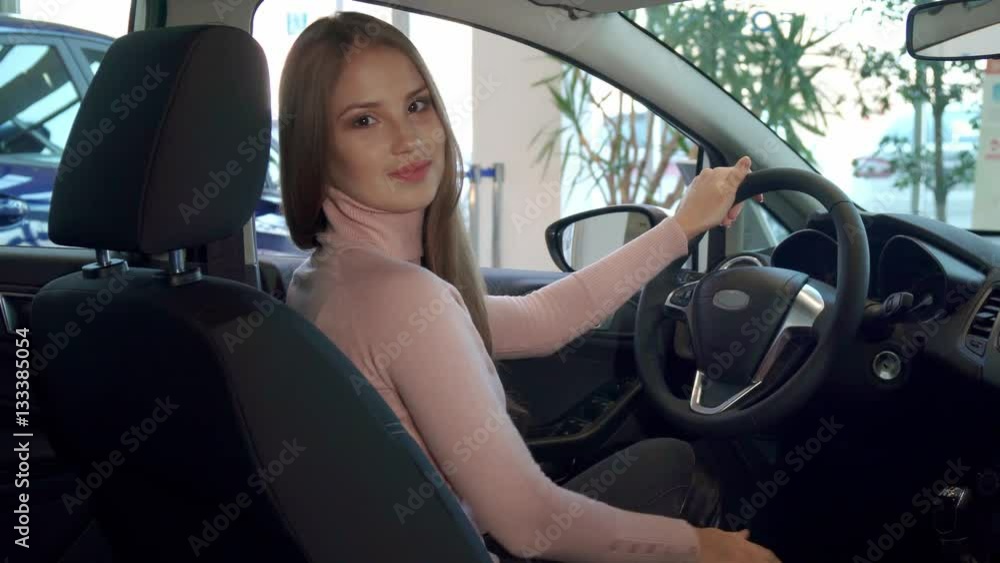 Pretty caucasian woman showing her thumb up inside the car. Attractive brown haired girl touching the gear stick. Beautiful female driver turning her face to the camera Pretty caucasian woman showing her thumb up inside the car. Attractive brown haired girl touching the gear stick. Beautiful female driver turning her face to the camera