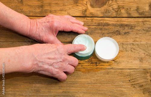 Old woman applying hand cream at home. Close-up of wrinkled woma