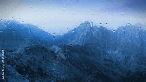 raindrops on a window with bluish mountainous landscape outside