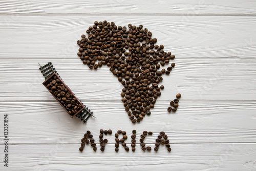 Map of the Africa made of roasted coffee beans and toy train on white wooden textured background with space for text