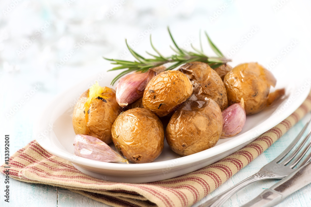 Oven baked potatoes or jacket potatoes with rosemary and garlic cloves on a white plate Oven baked potatoes or jacket potatoes with rosemary and garlic cloves on a white plate