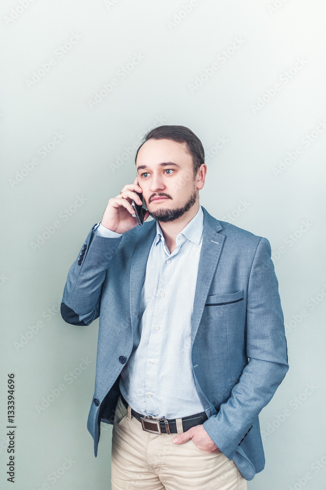 Young man talking on the phone in a denim jacket on gray background