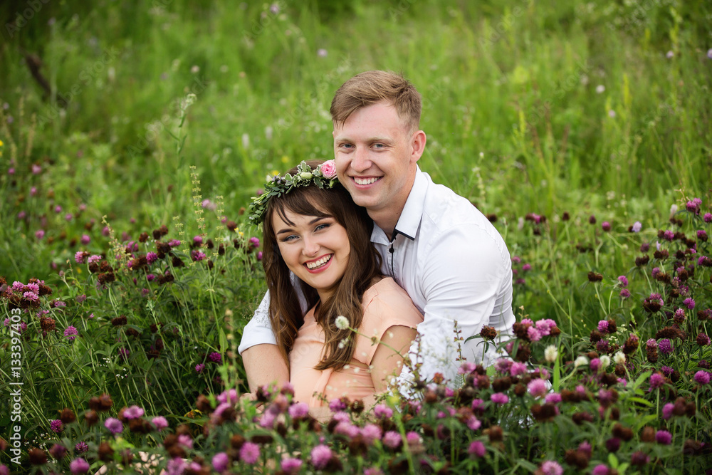 Happy couple, young woman and man hugging in field of flowers and looking to camera with smile on face. Love concept