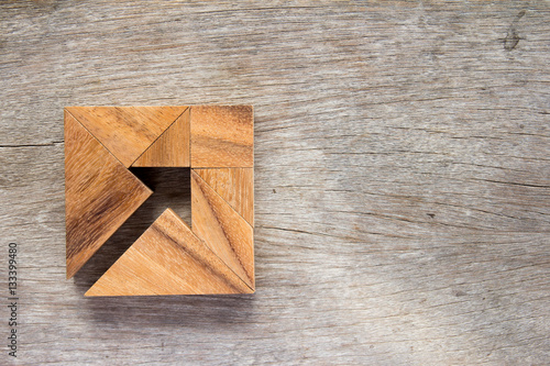 Tangram puzzle as arrow in square shape on wooden background