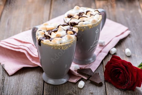 S'mores drink. Two mugs of hot chocolate with marshmallows on a wooden table. Cocoa. Rose petals. Valentine.