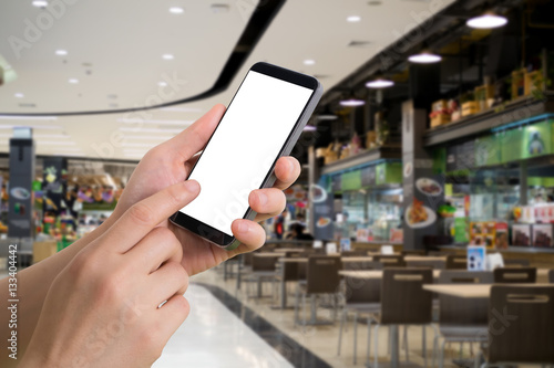 human hand hold and touch smartphone, tablet, cell phone with blank screen on blurred food court background.