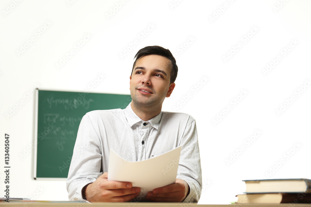 Handsome young teacher sitting at table in classroom Handsome young teacher sitting at table in classroom