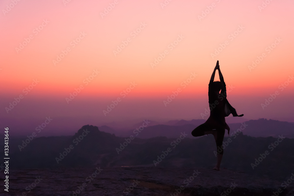 Silhouette young woman practicing yoga on the hill at dawn. Hampi, India