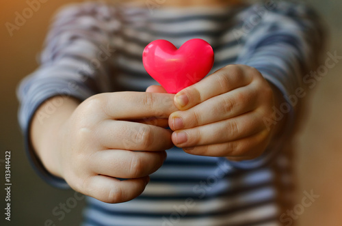 child holding a small pink heart. symbol of love, family, hope. Backgrounds for cards on Valentine's Day. Backgrounds for social posters about the preservation of the family and children. photo