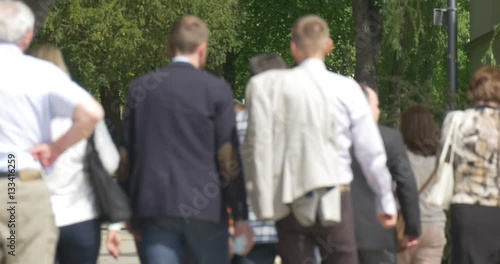 Group of Tourists is Moving Through the Park Backside View Backs of People Summer Green Trees Bushes People Are Listening to the Guide Walking Slowly