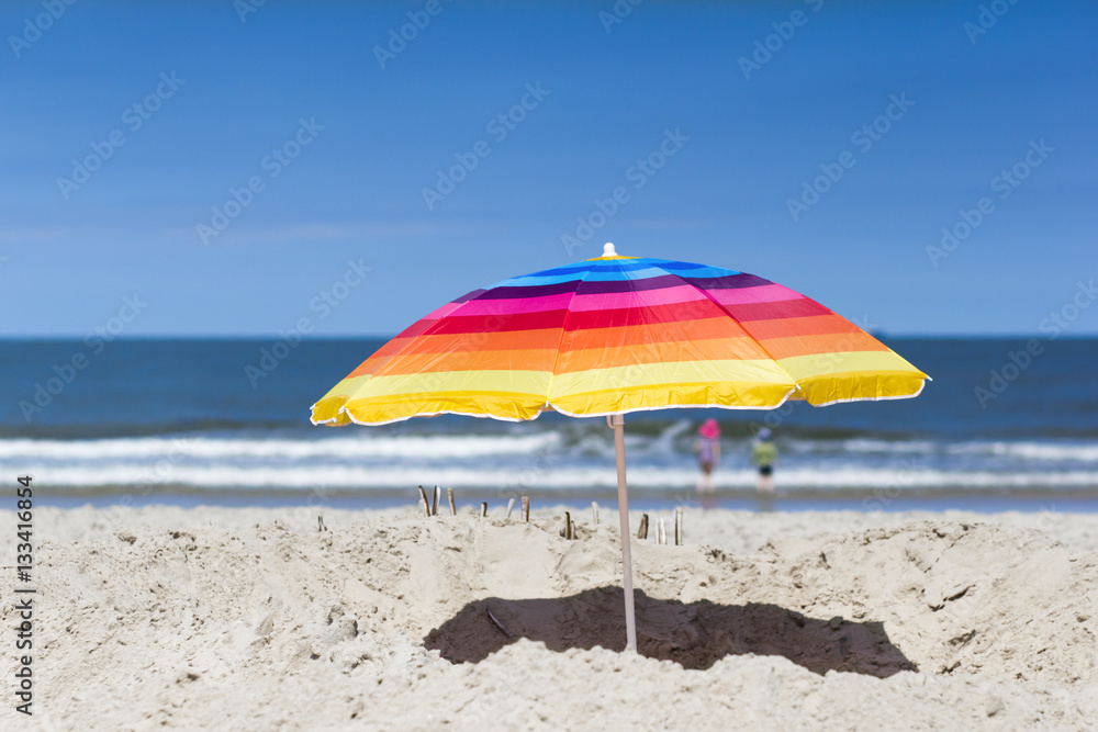 Colorful beach umbrella and two kids looking at the sea
