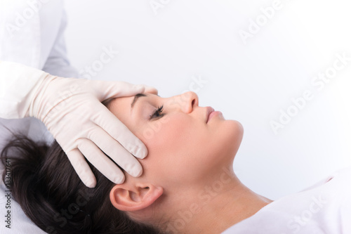 Beauty treatment of the young beautiful female face, doctor's hand in gloves touch face of beautiful young woman.