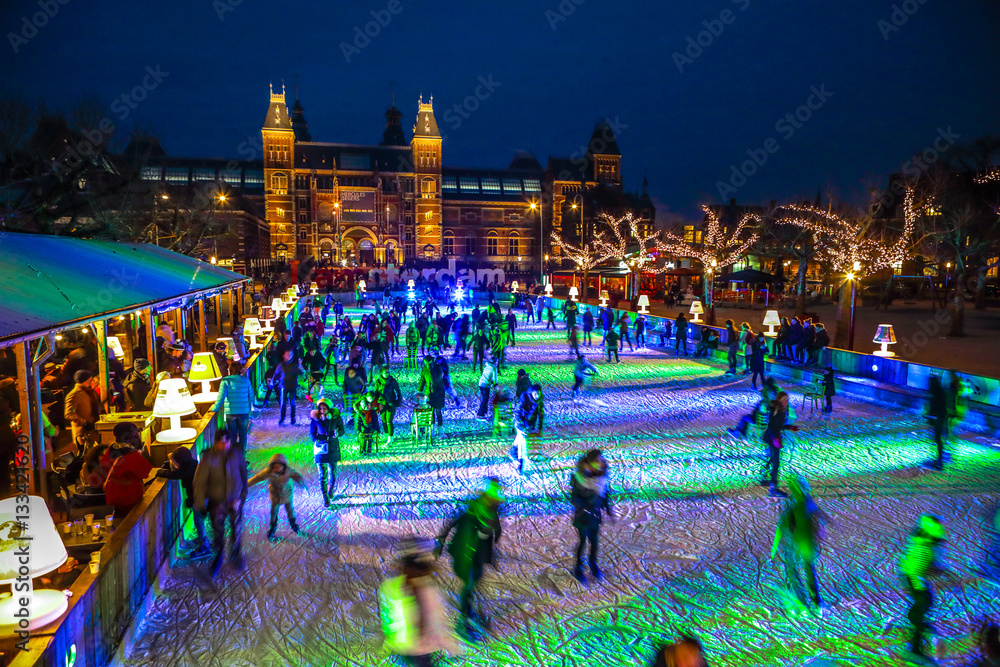 Fototapeta premium AMSTERDAM, THE NETHERLANDS - JANUARY 12, 2017: Many people skate on winter ice skating rink at night in front of the Rijksmuseum, a popular touristic destination in Amsterdam, The Netherlands.