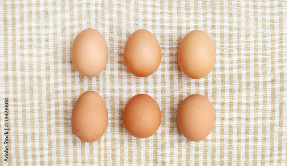 Six chicken eggs and wooden spoon on fabric on top shot Six chicken eggs and wooden spoon on fabric on top shot
