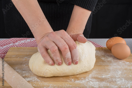 Hardworking female hands kneading dough on wooden kitchen table